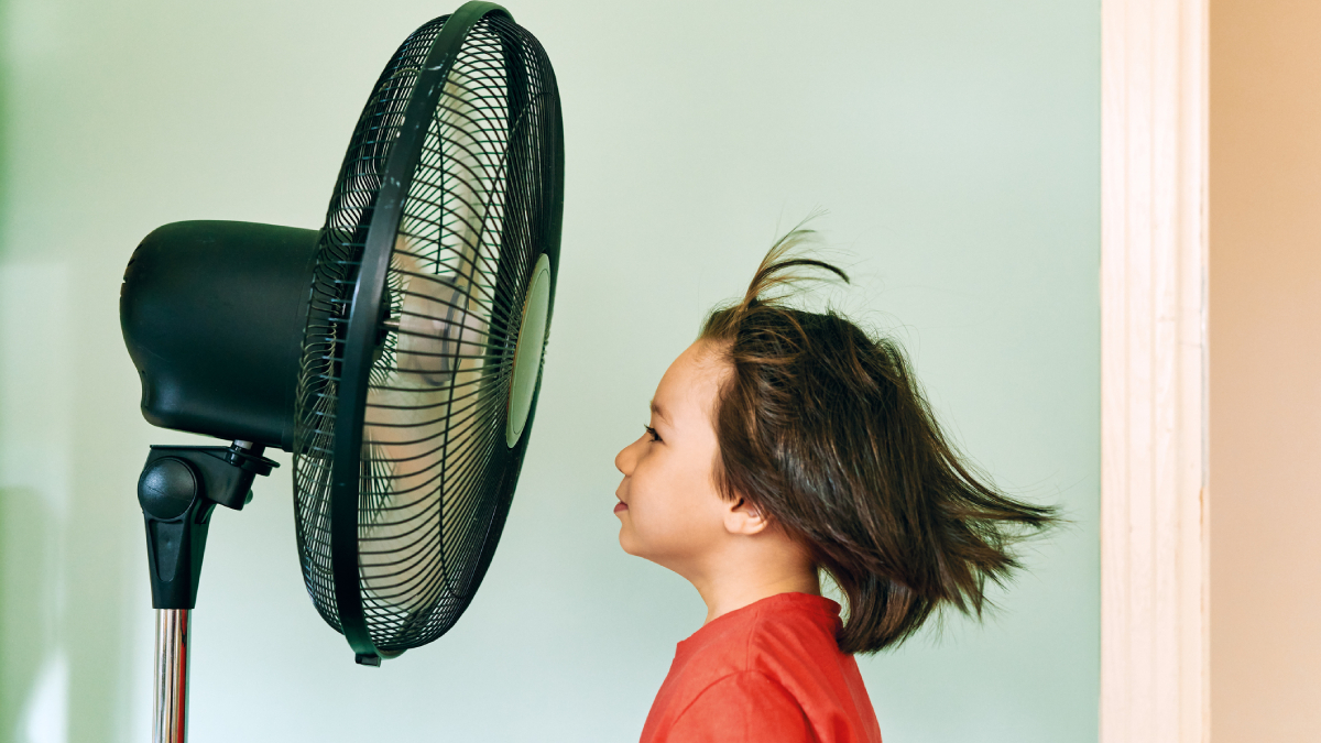 Child standing in front of floor fan blowing wind